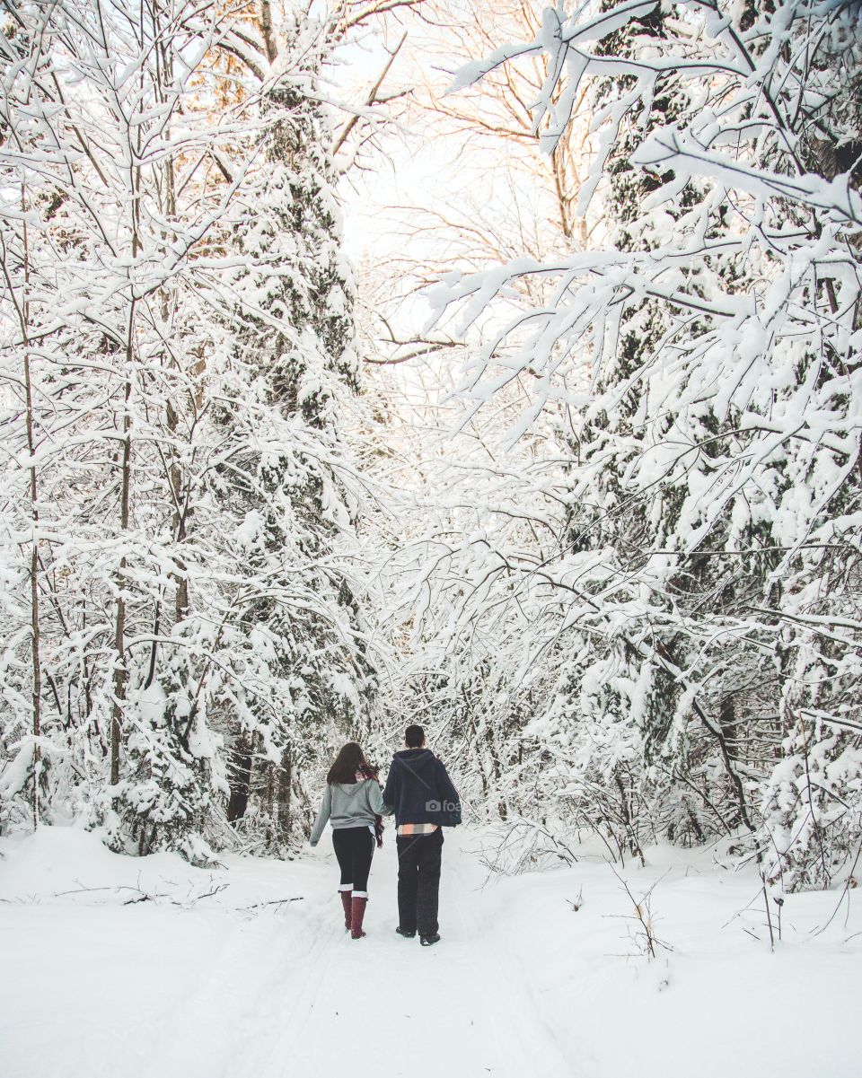 A young couple walking through a massive snowy forest on a tough hiking trail