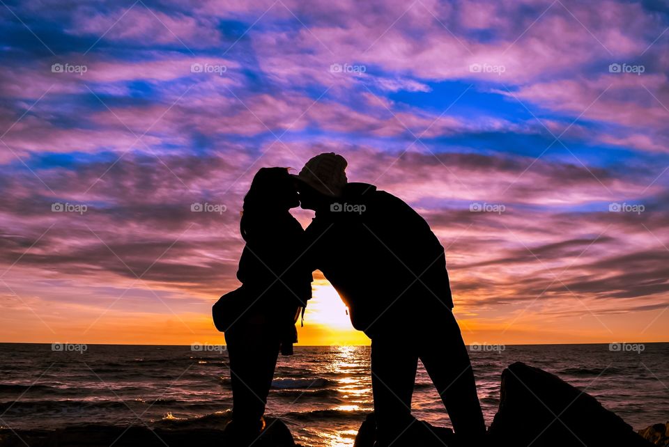 Sunset kiss!. Couple kissing by the sea at sunset, golden hour with beautiful dramatic sky cloud 