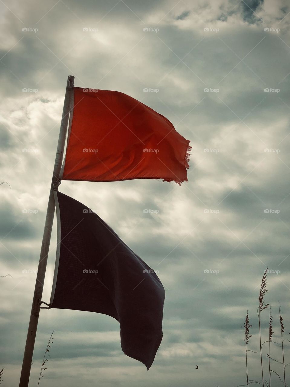 Red and purple warning flags whipping in the wind against a cloudy, stormy looking sky. A riptide is likely at the beach today.