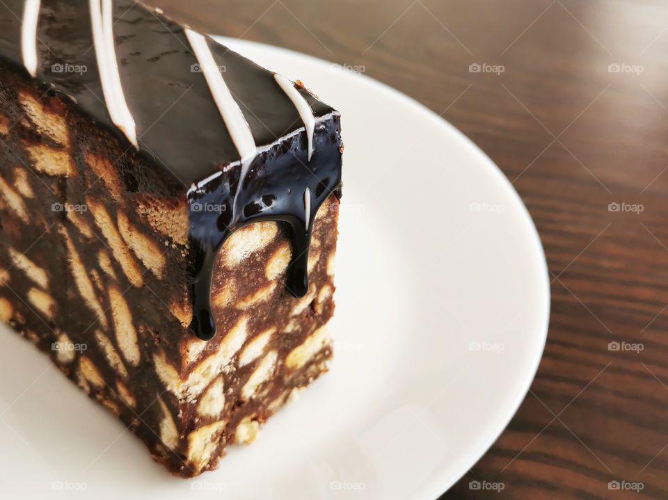 Chocolate cake on a white plate with copy space on the right side. Selective focus at the melted chocolate ganache that falling down on the cake.