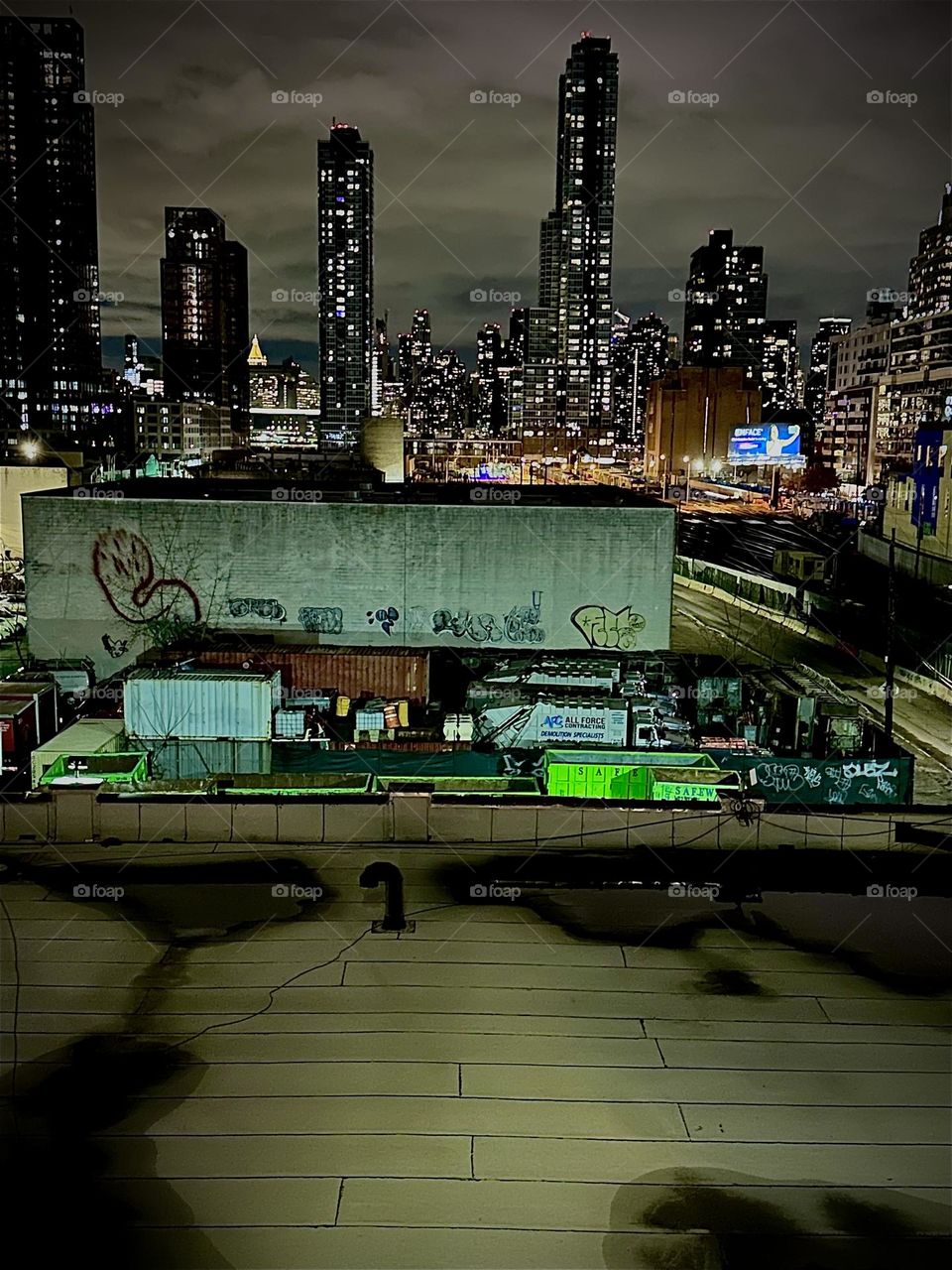 This is the view from the top of the “Pulaski Bridge” at “Newtown Creek” in LIC, Queens. We overlook adjacent flat rooftops, the train tracks of the “Long Island Railroad” and the skylines of LIC and “Manhattan”. 2023. Hypnotic Productions