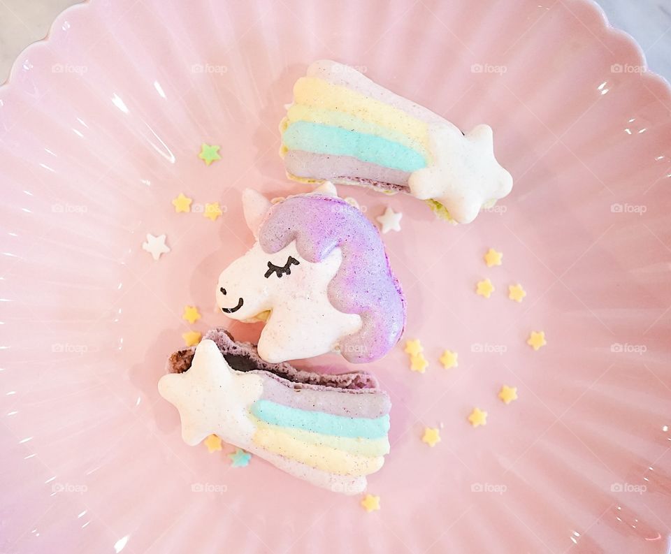 Unicorn macaron and pastel rainbow macarons on the pink dish with starry sugar, top view. Fairy tales and fantasy concept.