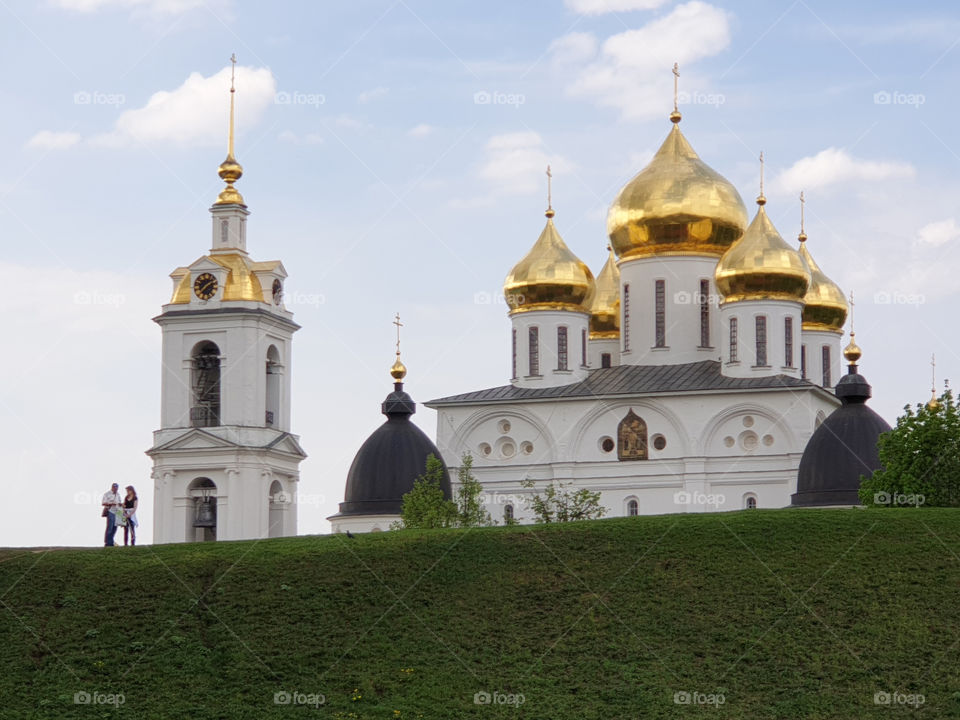 Russia. Dmitrov Kremlin.. Tourists man and woman studying the map against a clear sky, a beautiful white Orthodox Church with Golden domes and a bell tower in summer on a clear Sunny day