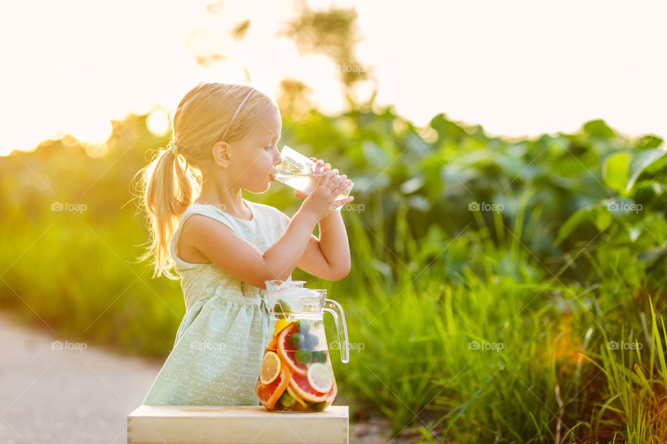 Cute little girl with blonde hair drinking lemonade outdoor 