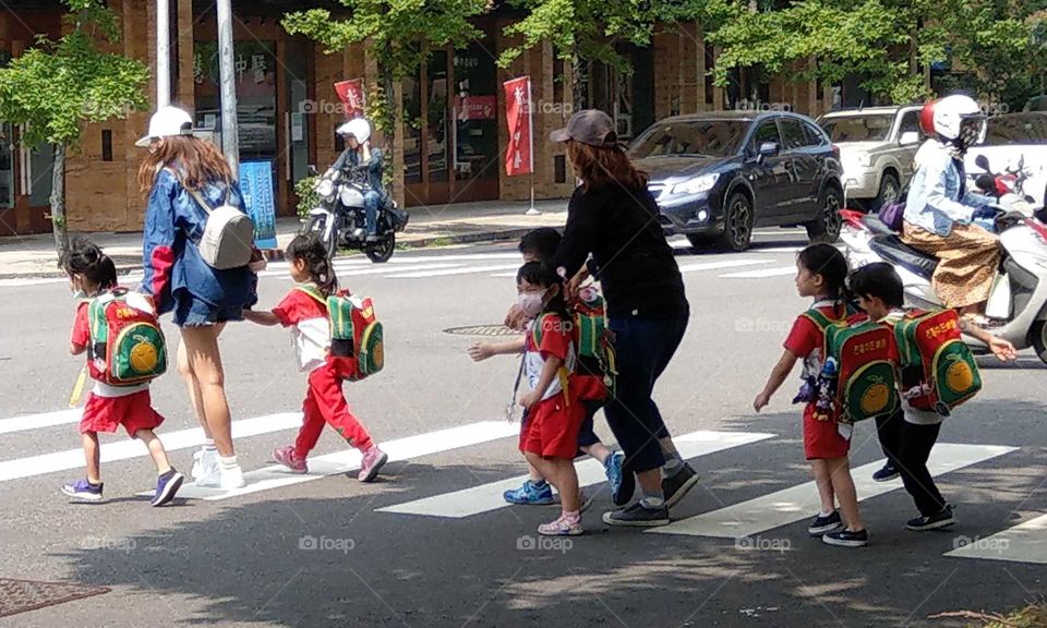 The kindergarten children cross the street, two teachers have a q warm behavior for protecting children. so cute and lovely.