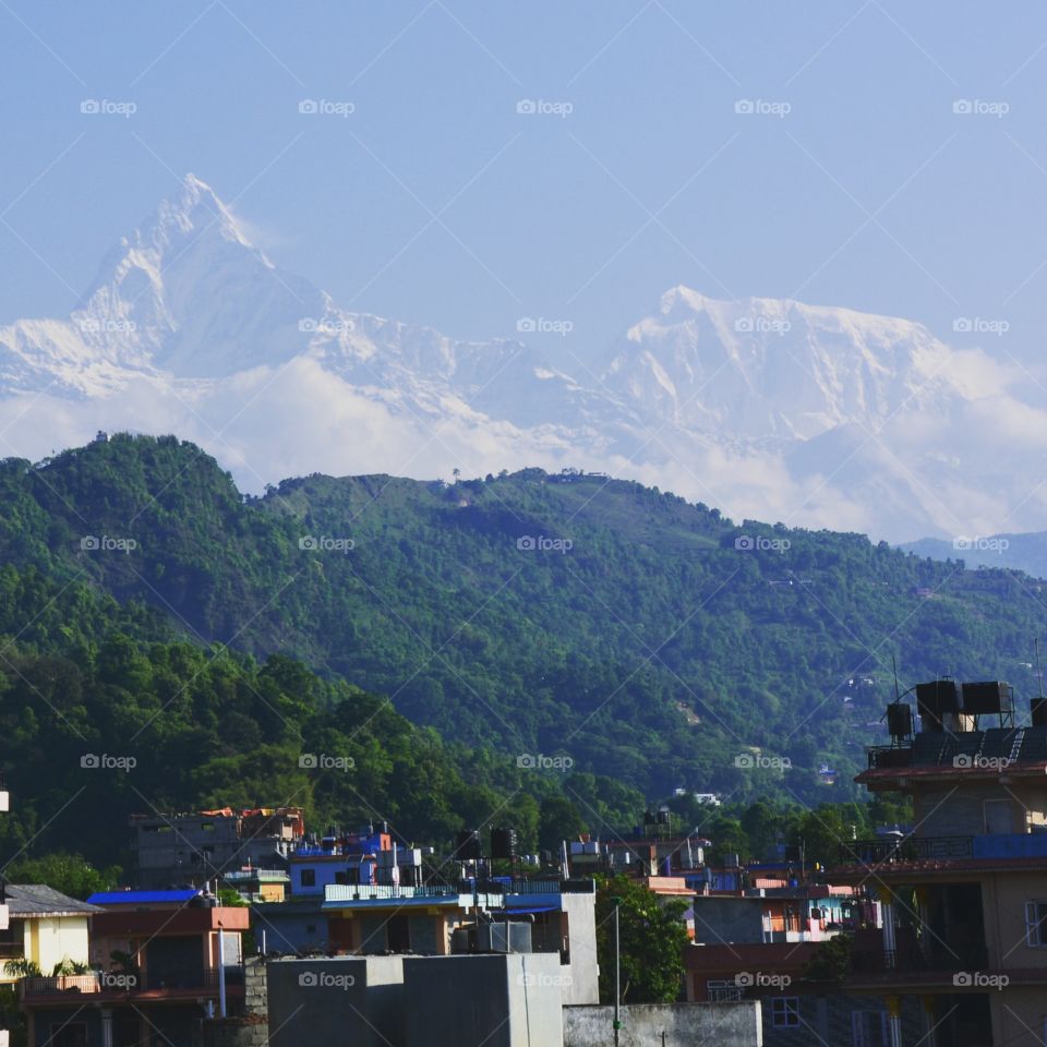 mountains in the distance over a green hill and a small neighborhood in Nepal