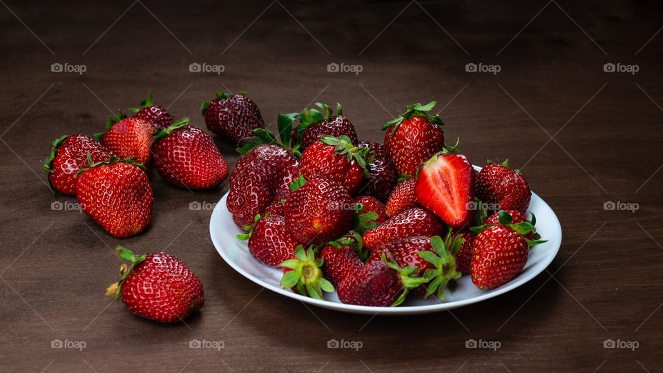 Fresh strawberries in ceramic bowl on dark wooden background. Selective focus.