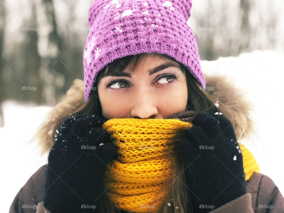 Winter portrait of a young woman cuddling in yellow knitted scarf 