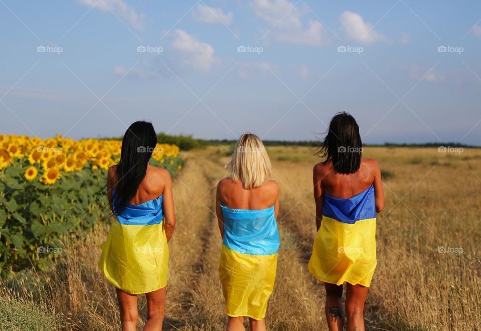beautiful girls, turned into yellow-blue flags, walk near the field with sunflowers