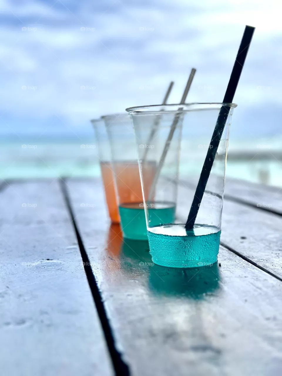Three colorful drinks in clear plastic cups with straws on a table in a beach front cafe