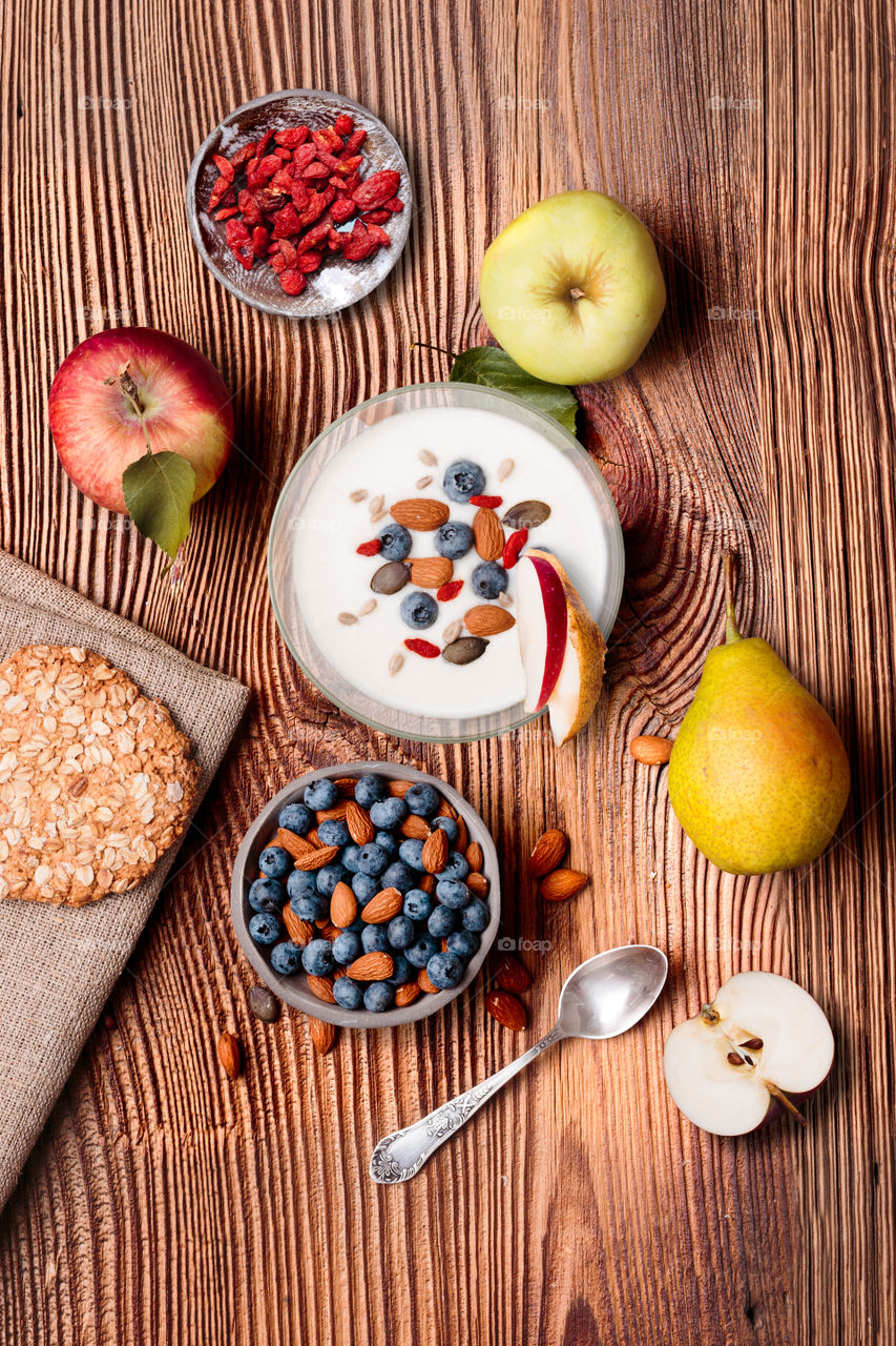 Breakfast on table. Yogurt with added blueberries and roasted almonds. Muesli cookie, apples and pears on wooden table. Light and healthy meal. Good quality balanced diet. Flat top-down composition