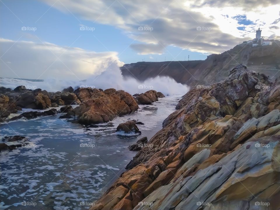 Waves breaking on rocks with lighthouse in the distance