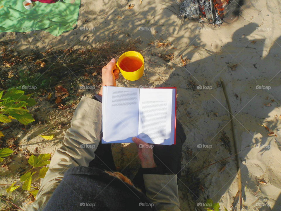 the girl is reading a book and is having tea in the open air