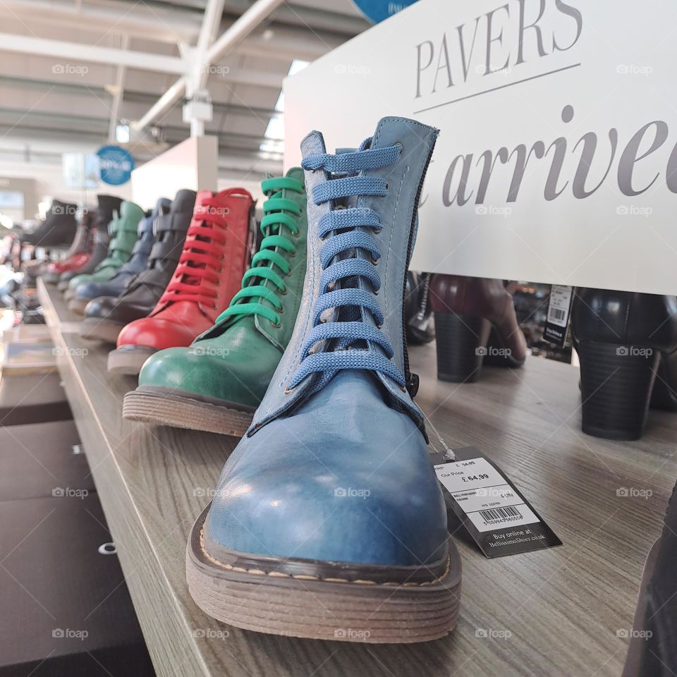 different coloured boots in a row on a display shelf in a shoe shop to buy