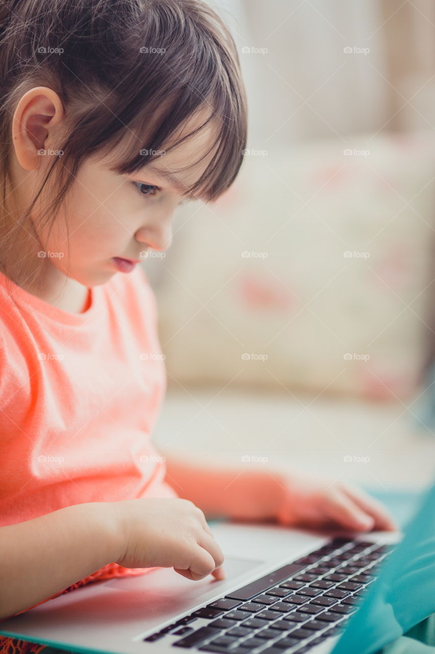 Little girl with gadgets(laptop and tablet) in the bed.