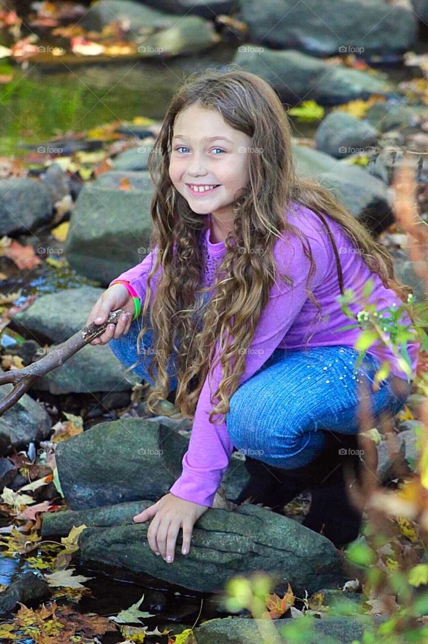 Cute girl holding stick and sitting on stream