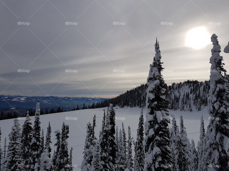 Sun behind the clouds over a lake on the side of a mountain, Big White, Canada