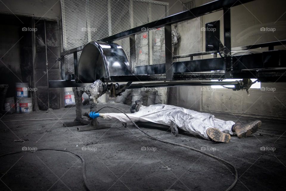 A hard-working person painting the undercarriage of a trailer frame.