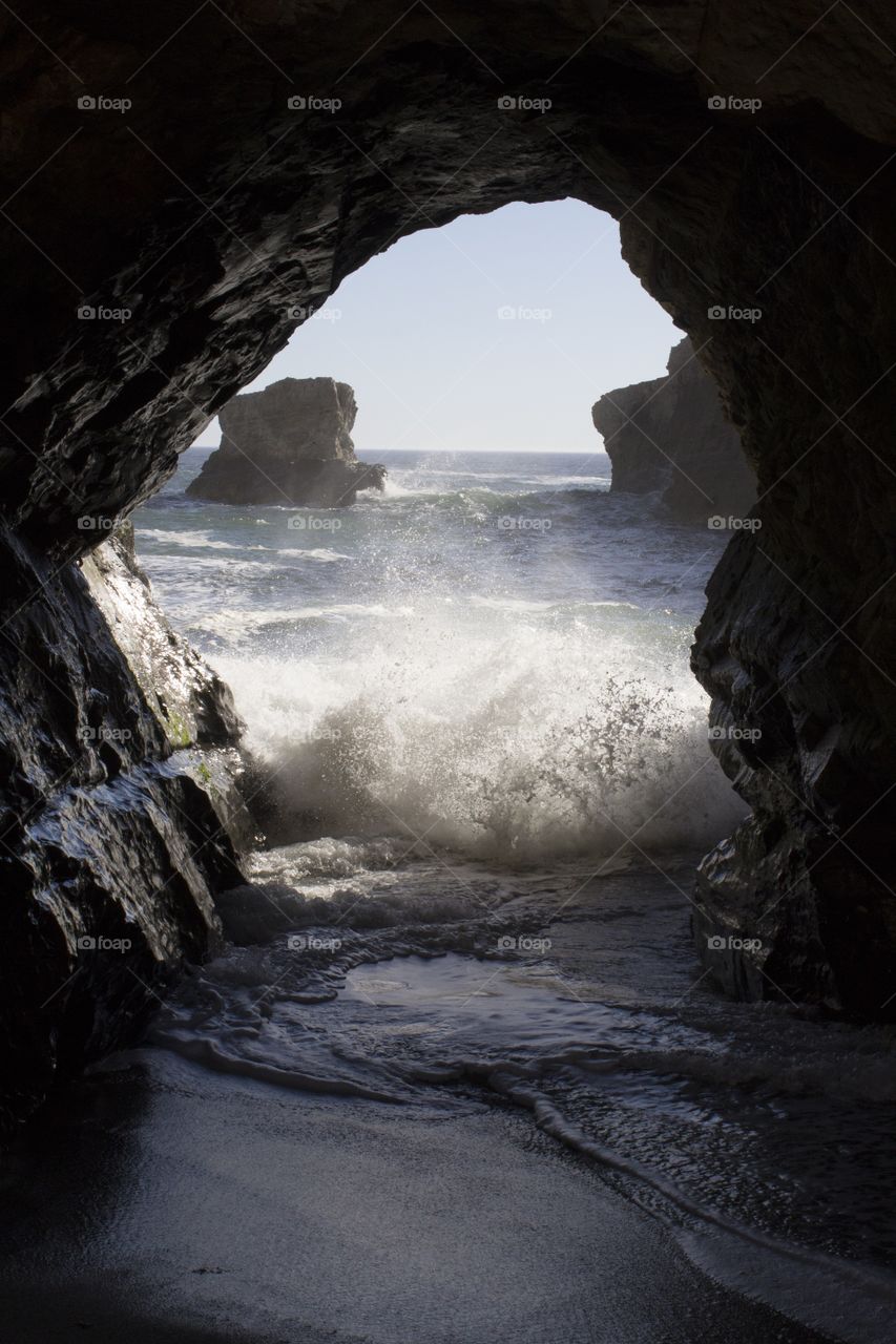 Gentle waves crashing through a small sea cave at low tide at Sharktooth Beach in Davenport, California on a clear, bright sunny day