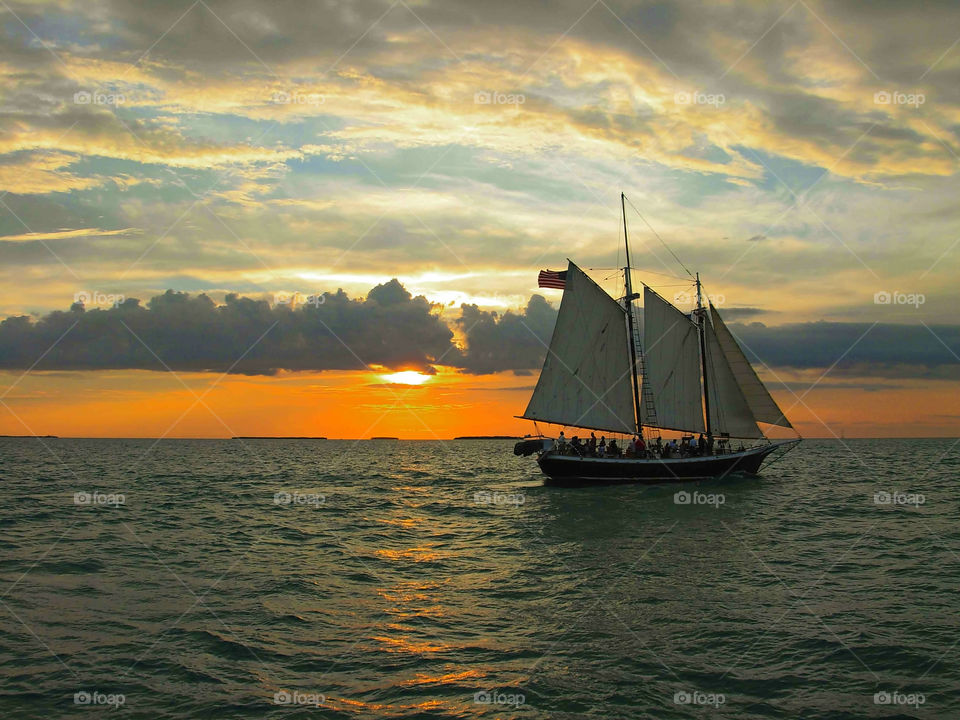 Sailing Boat Blue Orange Sky. Boat sailing in ocean against backdrop of golden light as sun is about to set