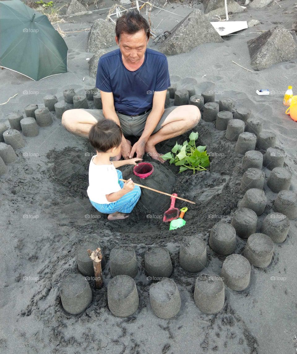 The memories of summer: grandfather and grandson playing sand and cooking at beach summer dusk. a scene of happiness, also a memory of happiness.