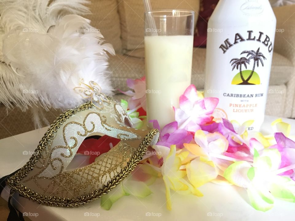 Venetian masquerade mask with a piña colada drink with a bottle of Malibu flavoured with pineapple liquor and flower garlands 