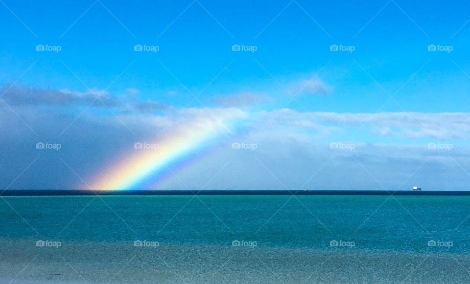 Bright rainbow full of colour over the sea ship in background 