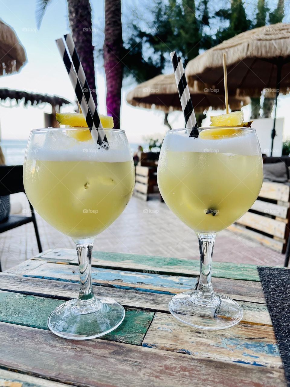 Yellow colored cocktails on wooden table with beach and sea in the background 