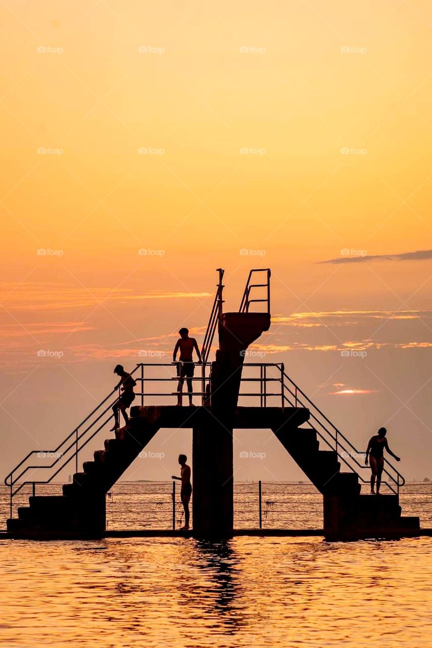 Young people on the mettalic diving platform in Saint Malo at sunset