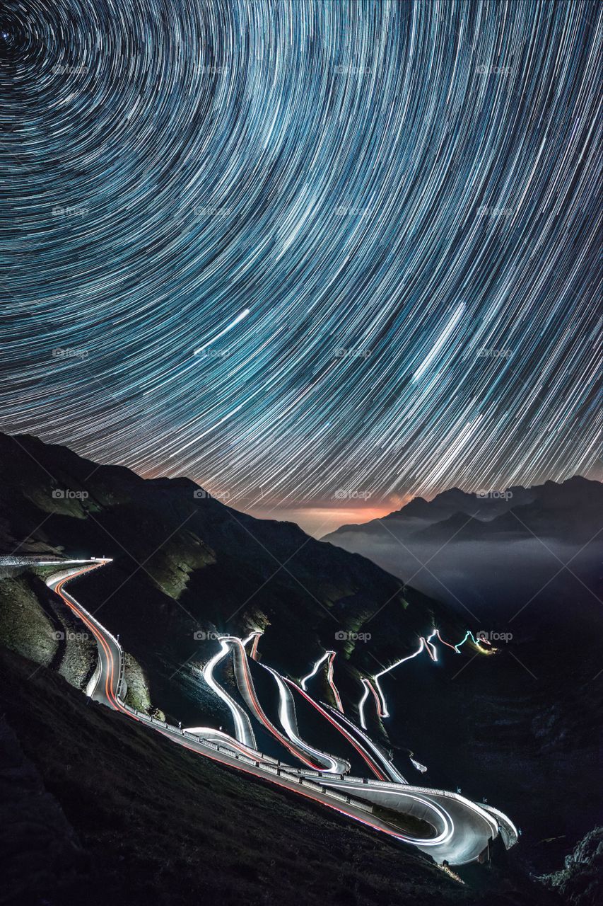 a time-lapse shot of a winding highway, starry sky and mountains making a brightly-lit effect
