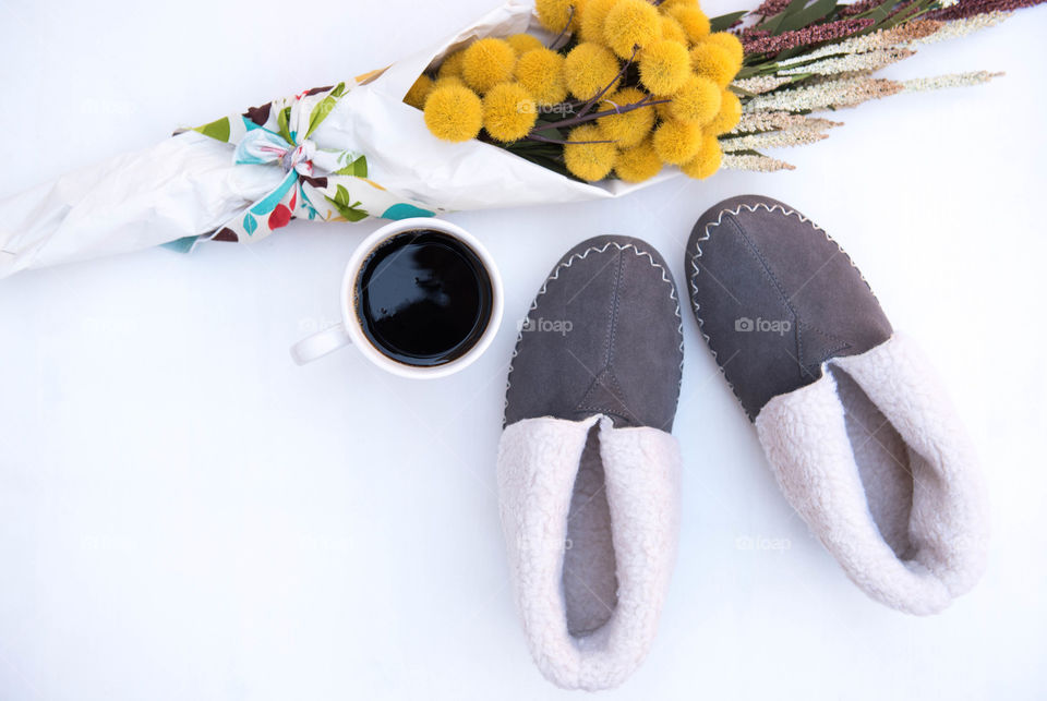 Flat lay of a pair of slippers, bouquet of flowers and a cup of coffee on a clean white floor