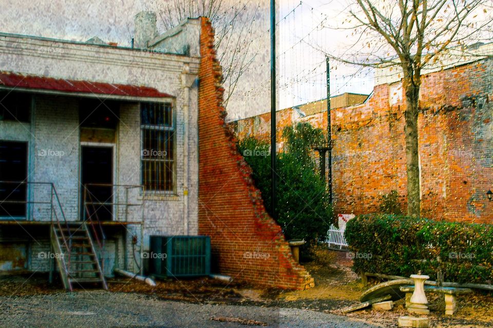 A building that has started to fall apart sits next to an alley of newer buildings decorated with Christmas lights 