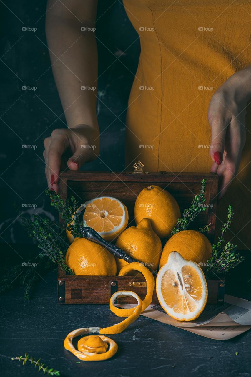 A conceptual image of vitamins. A girl in a yellow dress stands behind a casket full of ripe lemons. Proper nutrition and attention to sufficient consumption of fruits and vegetables. Yellow interior poster.