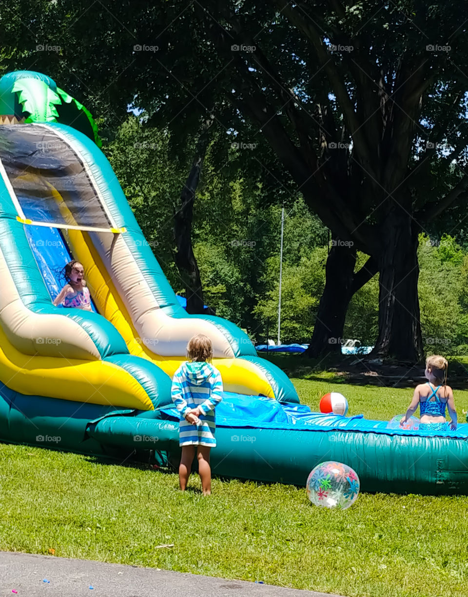 Child sliding down inflatable water slide screaming with excitement while other children look on.