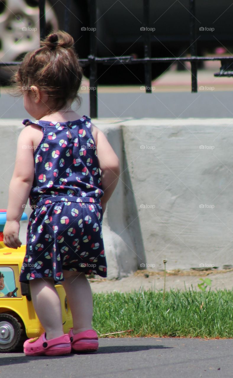 Toddler girl with hair bun wearing pink crocs playing with Little Tikes car 