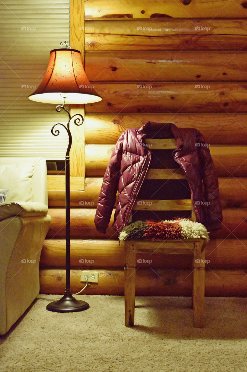 Still life. A lamp, a chair with a jacket on it and fluffy seat in a cabin. Orange, beige, plum colors. Wood log wall
