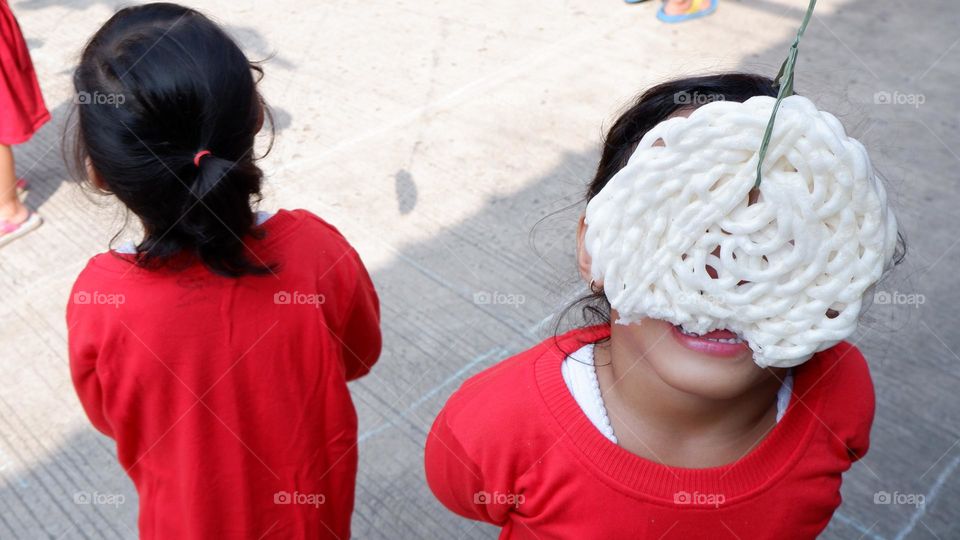 2 little girls in red dresses take part in a cracker eating competition that is hung and tied with rope.