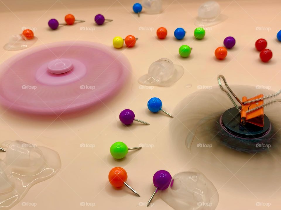 Two Fidget Spinners Time In Motion Long Exposure Seems To create Cold Ice Cubes Moving Pins Around On A Beige Background.