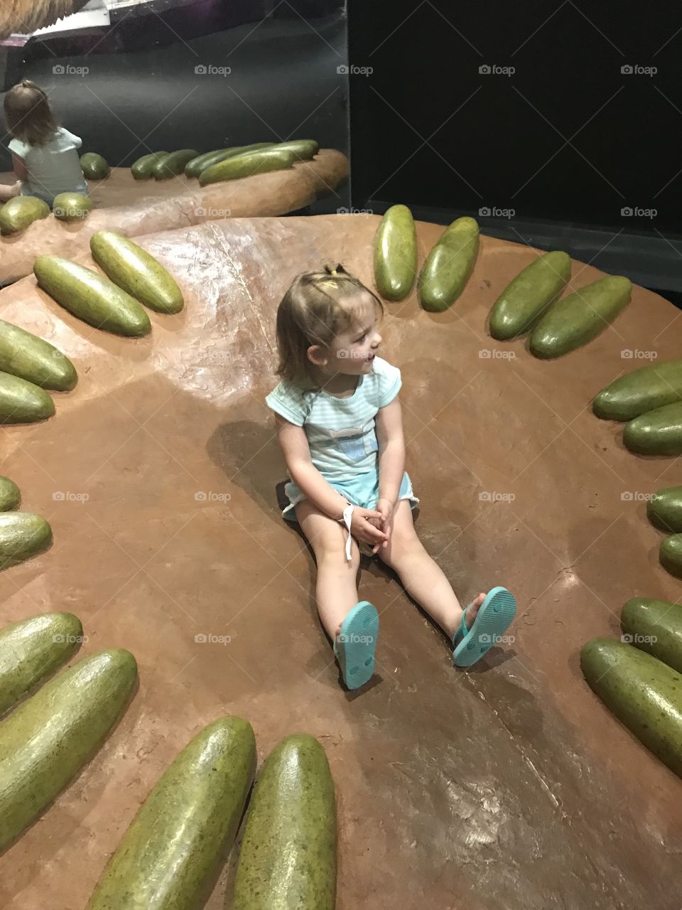 Toddler sitting in a dinosaur nest at the science museum, pretending to be a mommy dinosaur!