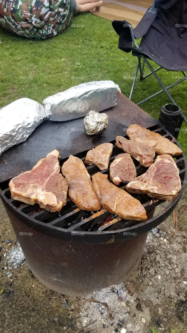 Juicy and delicious T-bone and Sirloin steaks cooking on the campfire. The perfect supper for summer camping.