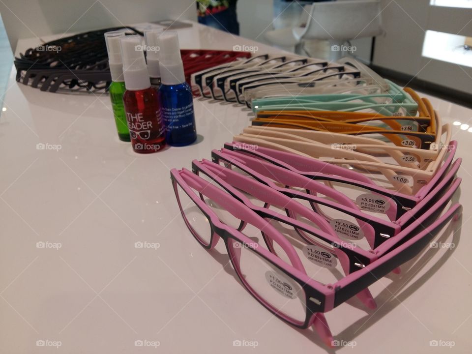 pink and colorful reading glasses displayed and arranged on white table with color bottles lens cleaner