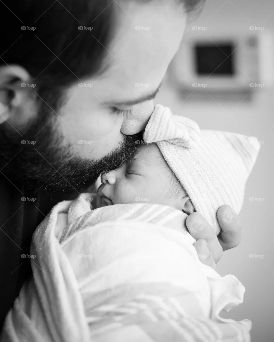 Father kissing delicate newborn daughter at the hospital after her birth in black and white.