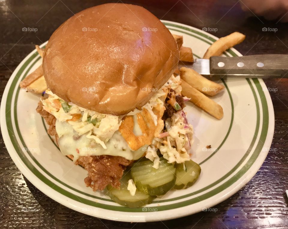 Huge chicken sandwich with coleslaw on top and pickles and fries on the plate beside the sandwich 