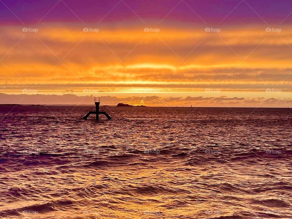 Sunset with a gradient of orange and purple over the sea at Bon secours beach in Saint Malo with the Bon secours mettalic diving platform on the horizon