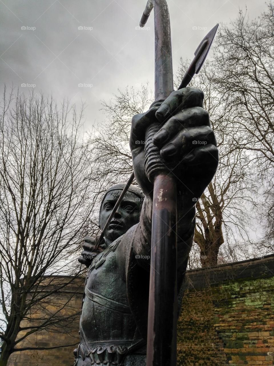 The Robin Hood statue in Nottingham, England.  In the background winter trees and cobblestone wall of the castle.