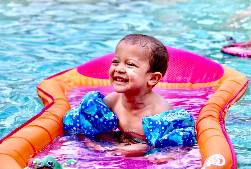 A cheesy smile from a toddler having fun in the pool