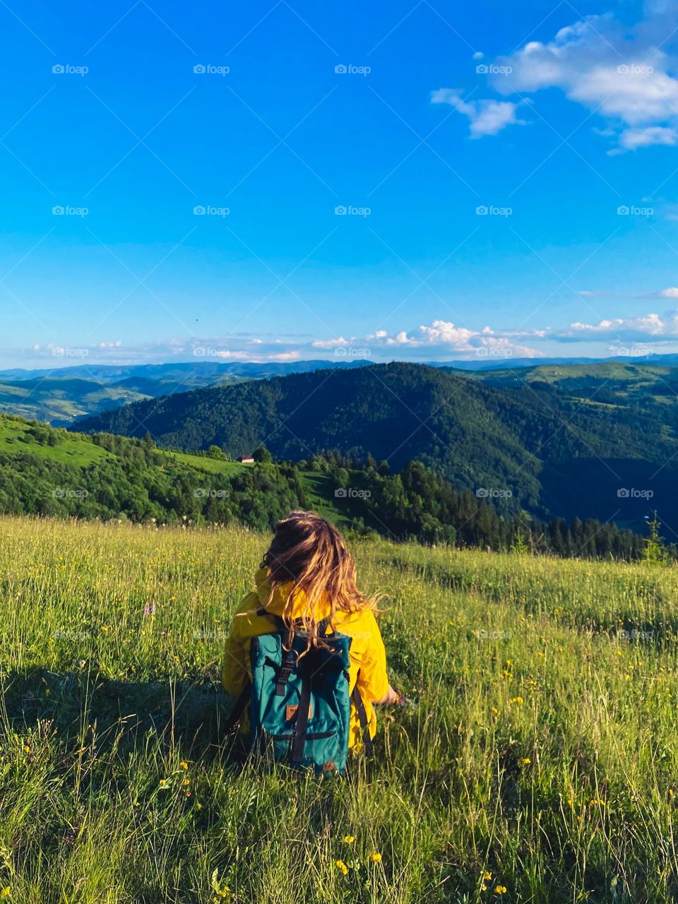 A girl in a yellow raincoat is sitting and watching at the mountains.