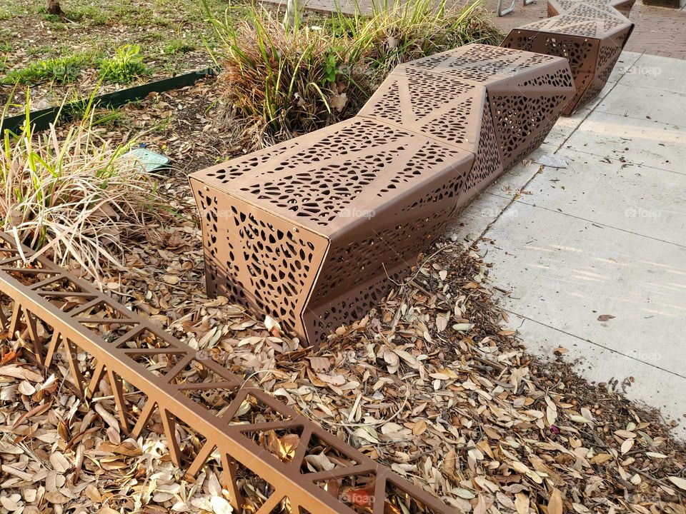 A unique artistic public bench and lighting cover made out of metal designed with triangle shapes.