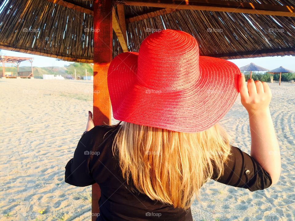 Back of woman with long blonde hair and red summer hat on the beach