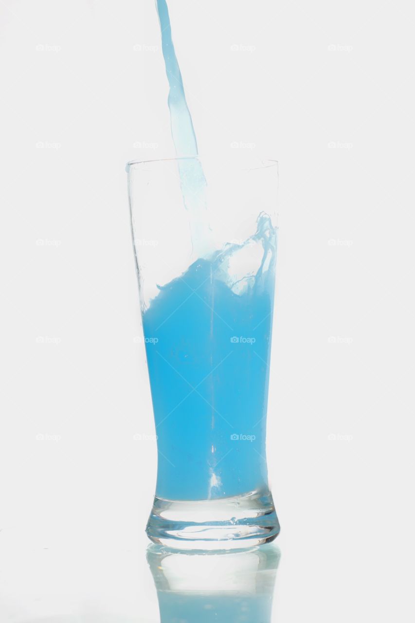 líquido azulado caindo em copo em superfície branca com um fundo Branco.